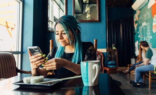 一个蓝头发的女人在餐厅吃寿司的时候在手机上.